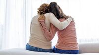 Rear view of mother and daughter embracing sitting on bed