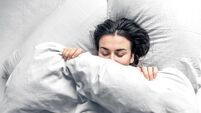 A beautiful young woman sleeps in a white bed.