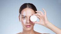 Studio portrait of an attractive young woman posing with a container of moisturizer against a grey background