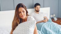Jealous unsatisfied girlfriend holding pillow and sitting on the bed while her husband using smart phone for reading or writing