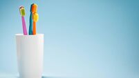 Three colourful soft toothbrushes in white mug on blue background
