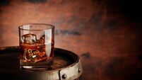 Glass of whiskey with ice cubes on the old barrel