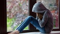 Sad girl in hooded top, sitting on a window ledge with head in hands in despair