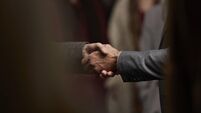 Close-up of 2 men making handshake in crowd