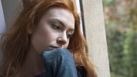 Portrait of worried girl looking through the window at home