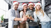 Positive multiethnic businesspeople in santa hats clinking with champagne in office